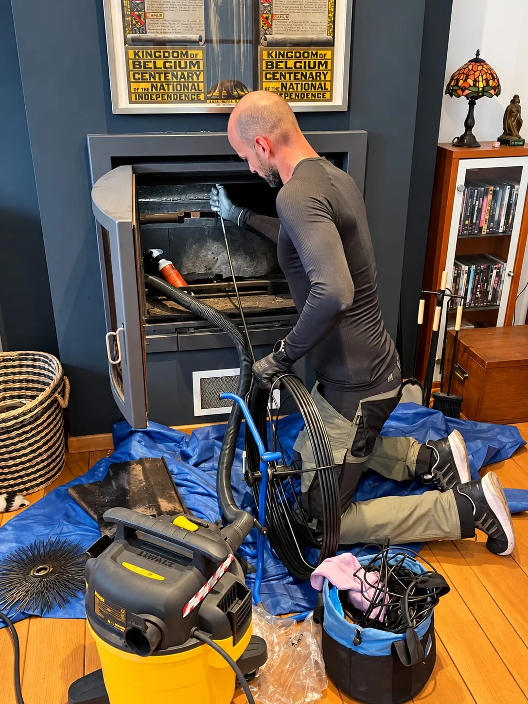 Ramoneur au travail devant un poêle, sol protégé par une bâche, aspirateur à suies et hérisson rotatif