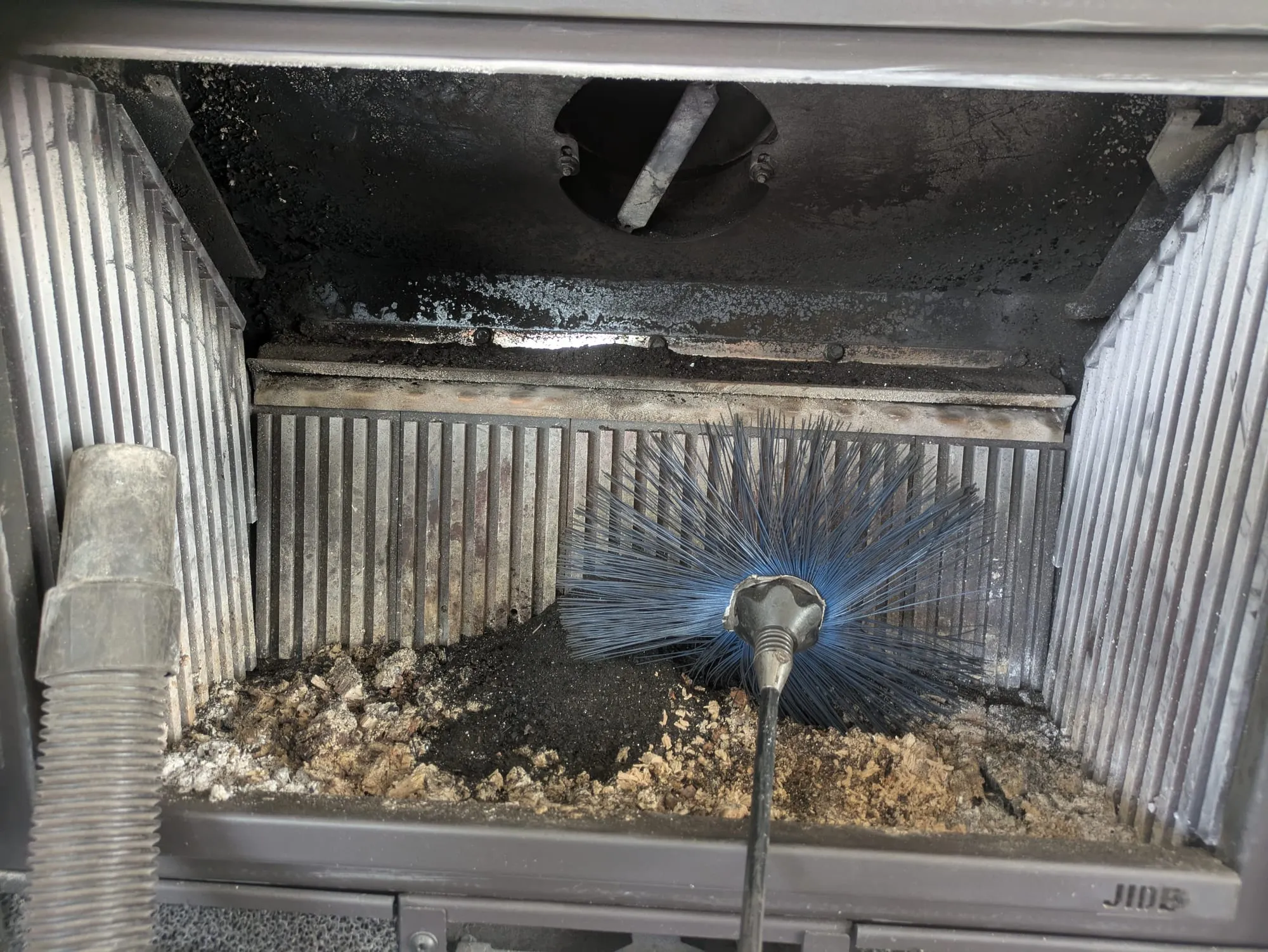 Hérisson de ramonage dans le foyer d'un insert, suies tombées du conduit